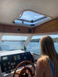 a woman sitting at the helm of a boat looking out over the water from inside