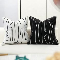 two black and white pillows sitting on top of a white couch next to each other