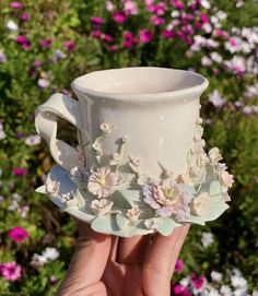 a hand holding a white cup with flowers on it