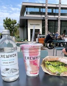 a person sitting at a table with a sandwich and drink in front of them on a sunny day