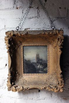 an old painting hangs on the wall in front of a white brick wall with a chain hanging from it