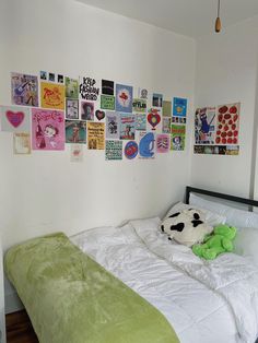 a white bed topped with a green pillow next to a wall covered in pictures and posters