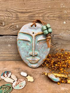 a ceramic mask sitting on top of a wooden table next to rocks and flowers,