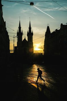 a person running down a street in front of a building with towers on it at sunset