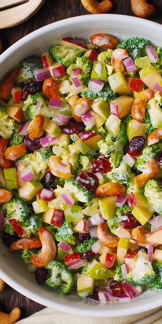 a bowl filled with broccoli, apples and cranberry salad on top of a wooden table