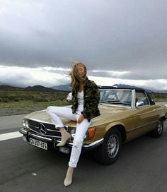 a woman sitting on the hood of a car in front of a brown mercedes benz