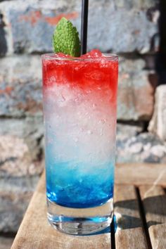 a tall glass with ice and a green leaf on the rim sitting on a wooden table