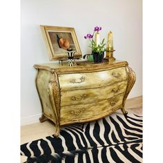 a gold dresser with flowers and pictures on it next to a black and white zebra rug