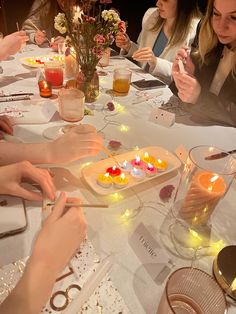 a group of people sitting at a table with candles in their hands and plates on the table