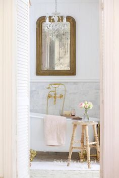 a white bath tub sitting under a mirror next to a table with flowers on it