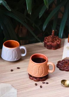 two coffee mugs sitting on top of a wooden table next to spoons and cookies