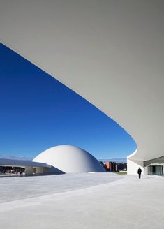 a person standing in front of a building with a blue sky behind it and people walking around