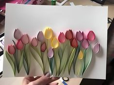 a person holding up a piece of paper that has flowers cut out of it and placed on a table