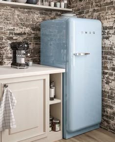 a blue refrigerator in a kitchen next to a brick wall and white counter top with dishes on it