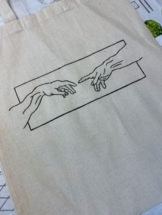 two hands touching each other on a tote bag that is sitting on a table