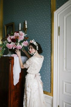 a woman in a white dress standing next to a dresser with pink flowers on it