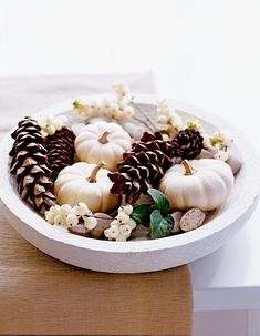 a white plate filled with pine cones and pumpkins on top of a wooden table