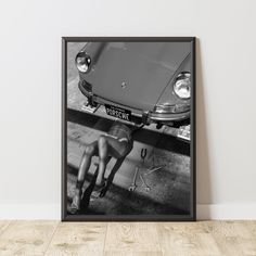 a black and white photo of a woman laying on the ground next to a car