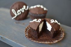 two chocolate cupcakes with white frosting and the word love on them sitting on a wooden table