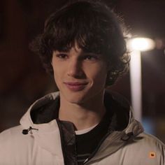 a young man with curly hair wearing a white jacket