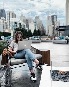 a woman sitting on a bench with a laptop in front of her and the city behind her