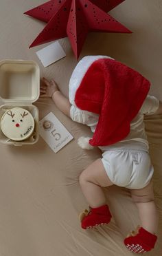 a baby wearing a santa hat and diaper next to a box with an ornament