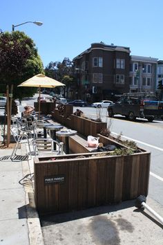 an outdoor seating area with tables and umbrellas on the side walk next to a city street