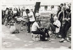 black and white photograph of people sitting on benches in front of a tree, with one man playing the piano