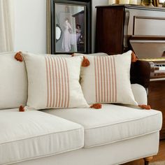 two white couches with orange and white pillows on them in front of a piano