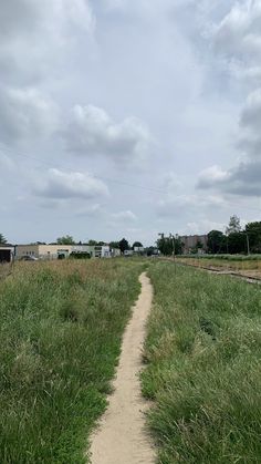 a dirt path in the middle of a grassy field with houses on either side and cloudy skies above