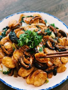 a white plate topped with fried mushrooms and green garnish next to chopsticks