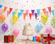 a birthday cake and presents on a table with balloons, streamers and confetti