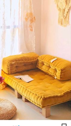 a yellow futon couch sitting in front of a window next to a vase with flowers