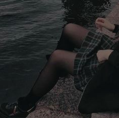 a woman sitting on the edge of a body of water with her legs crossed and wearing black shoes