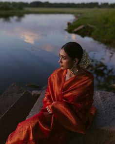 a woman in an orange sari sitting on the edge of a river at sunset