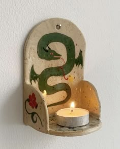 a candle holder with a green snake on it and a white wall in the background