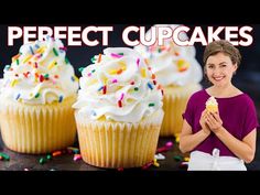 a woman standing in front of cupcakes with frosting and sprinkles