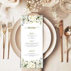 a table setting with white flowers and gold cutlery, silverware and menu cards