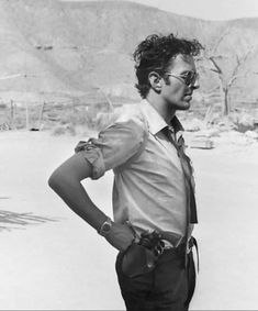 a man standing in the desert with his hands on his hips wearing glasses and a tie