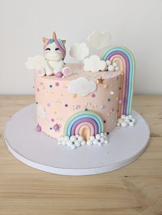 a pink cake decorated with rainbows, clouds and a unicorn sitting on top of it