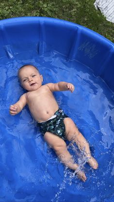 a baby laying in a blue pool with water on it's back and arms