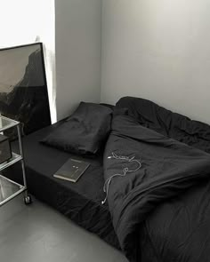 an unmade bed in a small room with a tv on the wall and black sheets