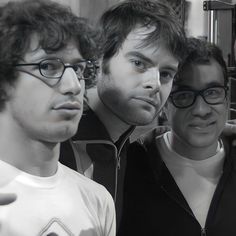 three men standing next to each other in front of a mirror with one man wearing glasses