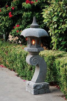 a light that is sitting in the middle of a sidewalk next to bushes and flowers