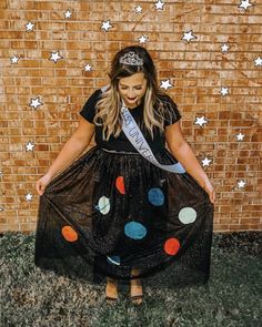 a woman in a black dress is standing by a brick wall wearing a tiara