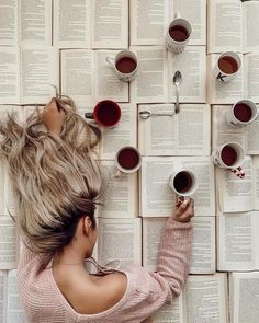 a woman laying on top of an open book next to cups of coffee