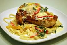 a white plate topped with pasta and chicken breast covered in sauce, garnished with red peppers