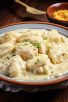 a white plate topped with dumplings covered in gravy next to a bowl of macaroni and cheese