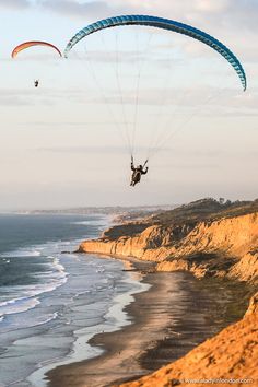 two people are parasailing over the ocean on a cliff near the beach and cliffs