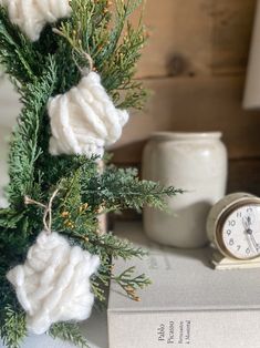 a clock sitting on top of a table next to a book and some pine branches